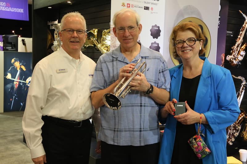 Belleville, Illinois residents William and Cynthia Shirley, winners of the Yamaha Silence is Golden contest winners, holding a SILENT Brass practice system for trumpet at the 2015 NAMM Show in Anaheim, California, the largest musical instrument trade convention in North America. During their all-expenses paid, four day and five night stay, the couple also visited Disneyland Park and Disneyland California Adventure Park. Standing to their left, Roger Eaton, director of marketing, Yamaha Corporation of America, Band & Orchestral Division.